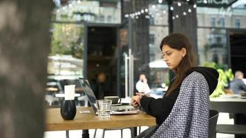 Young woman at an outside coffee shop table works or studies with laptop video