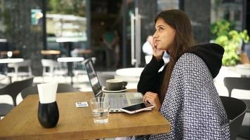 Young woman at an outside coffee shop table works or studies with laptop video