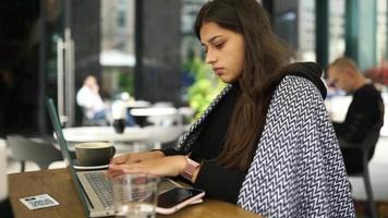 junge Frau an einem Kaffeetisch im Freien arbeitet oder studiert mit Laptop video