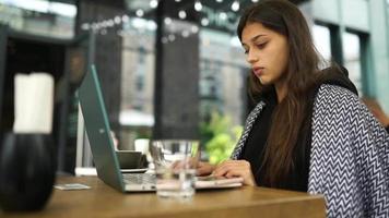 giovane donna a un al di fuori caffè negozio tavolo lavori o studi con il computer portatile video