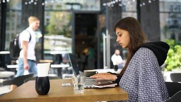 Young woman at an outside coffee shop table works or studies with laptop video