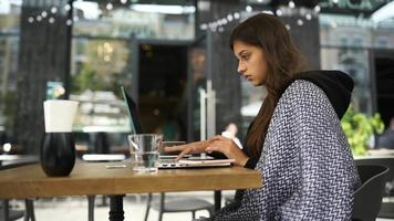 Young woman at an outside coffee shop table works or studies with laptop video