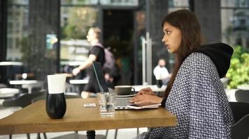 jovem em uma mesa de café externa trabalha ou estuda com laptop video