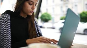 Young woman at an outside coffee shop table works or studies with laptop video