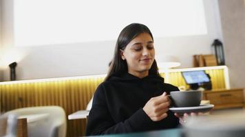 vrouw Bij koffie winkel slokjes van groot keramisch kop en glimlacht Bij iemand uit camera video