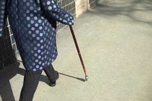 Grandma with walking stick. Woman walks on asphalt. photo