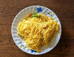 Closeup and top view fried Chinese noodle in white ceramic plate on wooden background. Thai and Chinese people popular eaten vegan foods in Chinese vegetarian festival in October every years photo