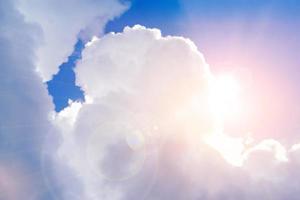 Big white cloud with sun and lens flare on bright blue sky. photo