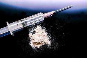 Plastic syringe put in a medical needle and white powder isolate on black background. Suppose to heroin or narcotic addiction. photo
