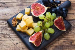 Cheese cubes, fresh fruit figs grapes Honey walnut on wooden chopping Board. Selective focus. Close up. photo