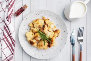 Fried cauliflower florets in batter on a white plate. White wooden background. photo