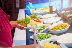 Asian woman choosing vegetable ingredients at salad bar restaurant photo