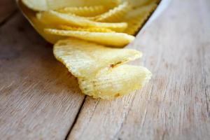 Opened pack with potato chips over wooden table photo