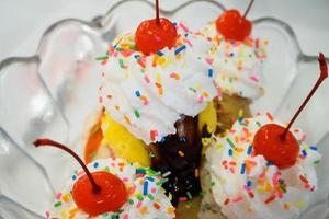 Cucharadas de helado con cereza y crema batida en recipiente de vidrio foto