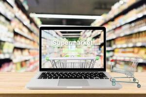 laptop computer on wood table with supermarket aisle blurred background online shopping concept photo