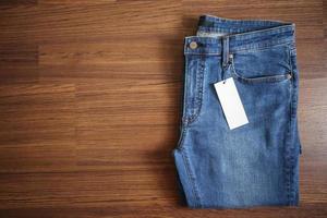 Blue jeans with blank white price label tag on wooden background photo