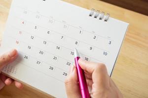 calendar page with female hand holding pen on desk table photo