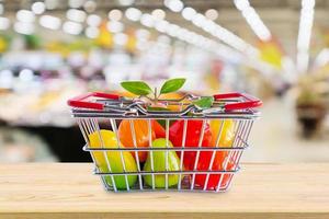 cesta de la compra con frutas en la mesa de madera sobre el fondo borroso del supermercado de la tienda de comestibles foto