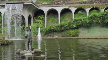 Waterfall feature and statue on stones in lush Monte Palace Tropical Garden in Madeira, Funchal, Portugal