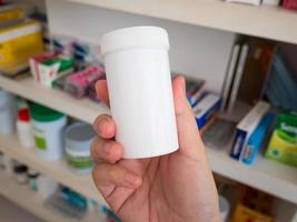 Close up pharmacist hand hold medicine bottles on shelves of drugs in the pharmacy photo