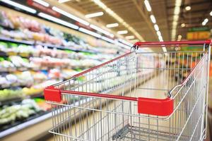 supermarket grocery store with fruit and vegetable shelves interior defocused background with empty red shopping cart photo