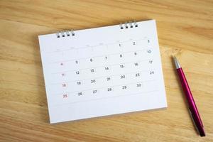 Calendar page with pen on wooden desk table photo