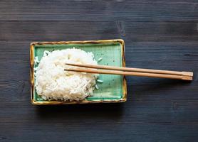 boiled rice with chopsticks on plate on dark table photo