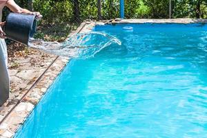 man pours of disinfectant from bucket in pool photo