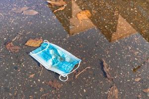 puddle with fallen leaves and used face mask photo