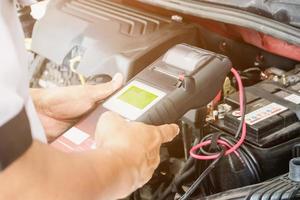 mechanic use voltmeter checking voltage of car battery in car service centre photo