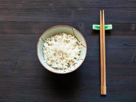 boiled rice in bowl and chopsticks on rest on dark photo