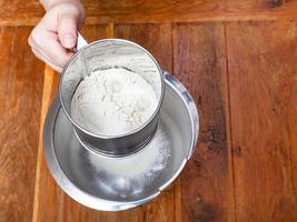 sifting the flour through sifter into steel bowl photo