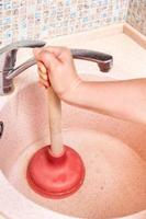 woman clears kitchen sink drain by plunger photo