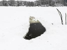 ice hole in frozen lake and view of park in winter photo