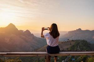 joven viajera tomando fotos con un teléfono inteligente al atardecer sobre la montaña