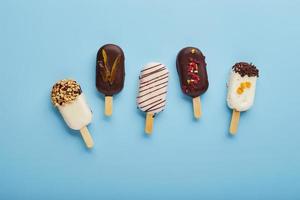 postre de mousse con sabores de frutas en forma de helado de paleta sobre fondo azul. foto