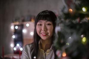 Cute dark-haired Korean girl in a cozy Christmas room with festive bokeh lights in the evening. Portrait photo