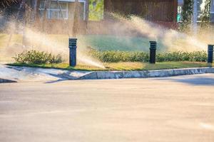 Automatic lawn sprinklers watering over green grass in the garden photo