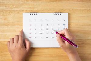 calendar page on table with female hand holding pen, top view photo