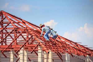 welder workers installing steel frame structure of the house roof at building construction site photo