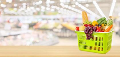 Shopping basket filled with fruits and vegetables on wood table with supermarket grocery store blurred defocused panorama background photo