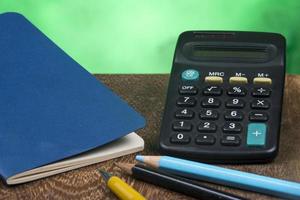 cuaderno con calculadora y algunos lápices en un banco y fondo verde foto