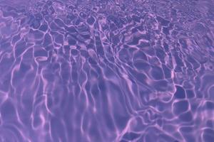 Defocus blurred transparent purple colored clear calm water surface texture with splash, bubble. Shining purple water ripple background. Surface of water in swimming pool. Tropical purple water color. photo