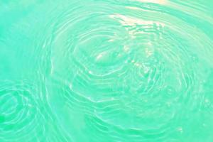 Defocus blurred transparent blue colored clear calm water surface texture with splashes and bubble. Trendy abstract nature background. Water wave in sunlight with copy space. Blue watercolor shining. photo