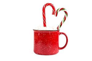 taza roja con malvaviscos y bastón de caramelo en forma de corazón sobre un fondo blanco aislado. navidad, año nuevo, ambiente festivo. foto