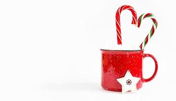 Red mug with marshmallows and caramel candy cane in the shape of a heart on a white background and a Christmas tree toy a wooden star. Christmas, New Year, festive mood. Copy space photo