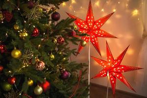 Red Christmas star-lamp on a stand. The festive decor of the interior of the house. Christmas, new year, spruce branches. Background, space for text photo