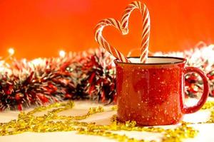 Red mug with striped candy canes in the shape of a heart on a red Christmas background with lights of garlands in bokeh. Copy space. New Year. photo