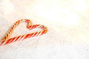 bastón de caramelo de navidad a rayas de santa en forma de corazón sobre una manta de punto blanca. un símbolo de amor, un regalo para un ser querido, un dulce regalo. Año Nuevo. espacio para texto foto