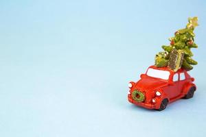 Christmas decor - a red retro car carries a Christmas tree with gift boxes on the roof. Toy with sequins on a blue background, space for text. New Year photo